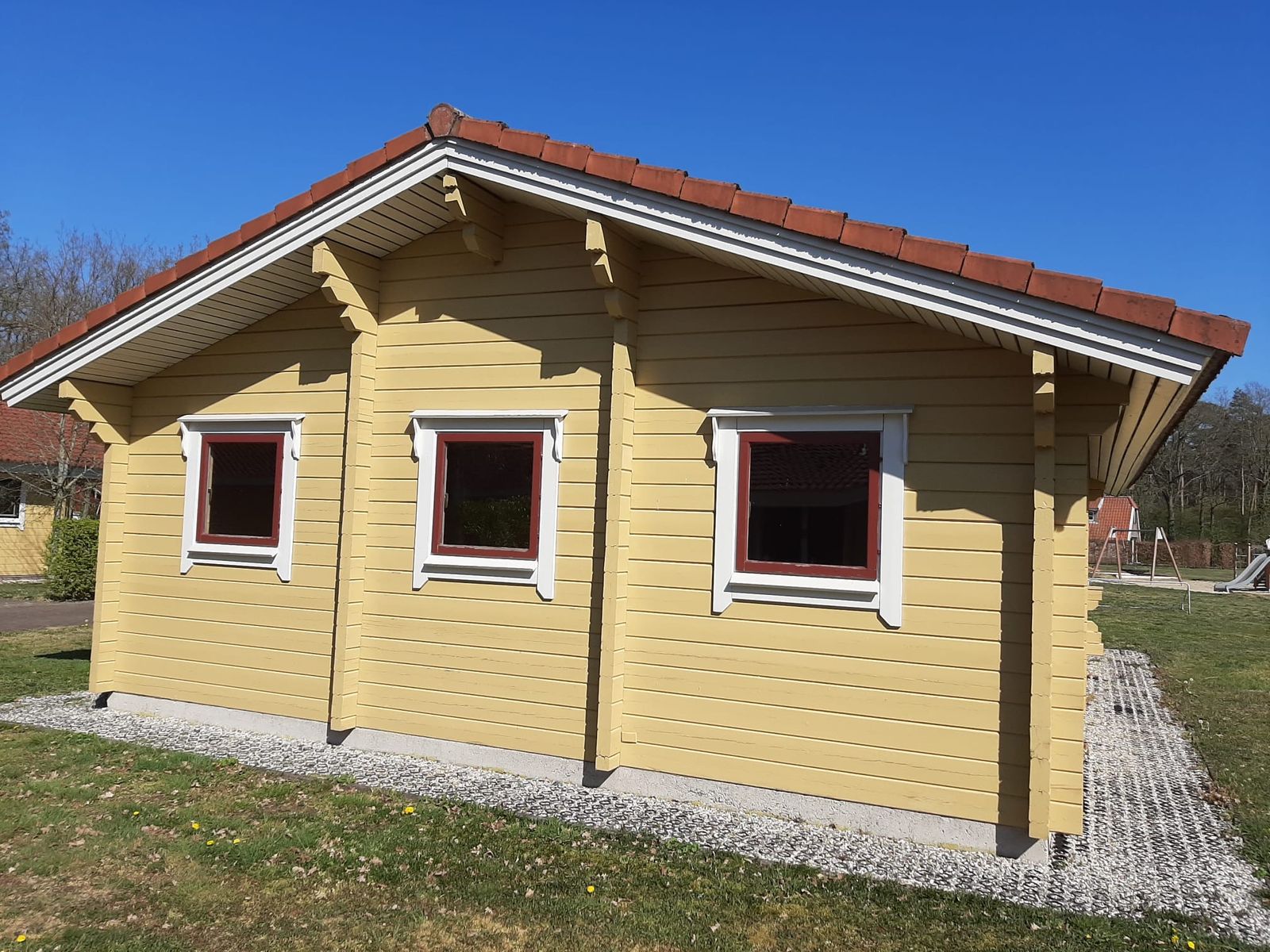 Geel geschilderd houten huisje met rode kozijnen