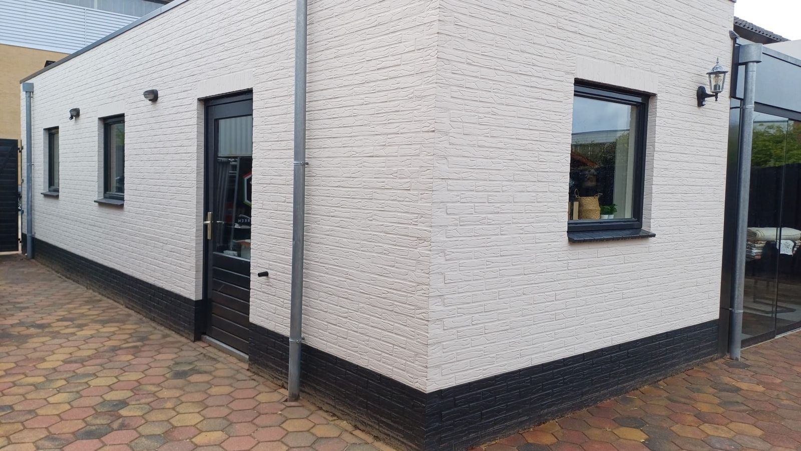 Wit geschilderd bijgebouw met zwarte plint