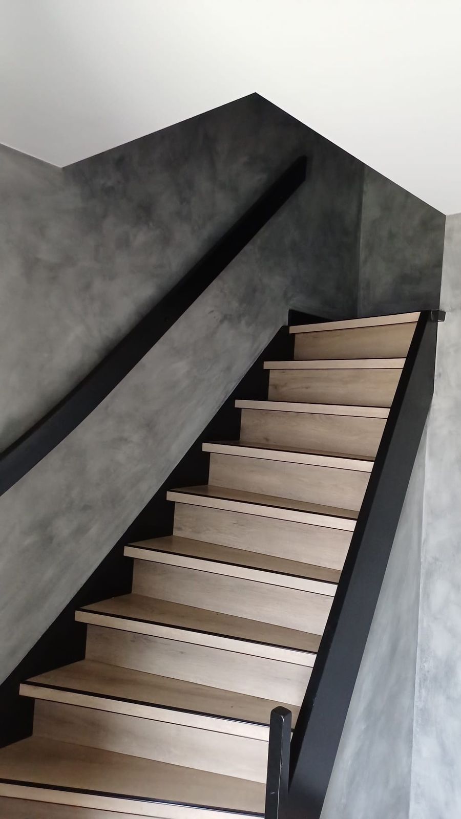 Zwart geschilderde trap met eiken treden tegen een betonlook wand